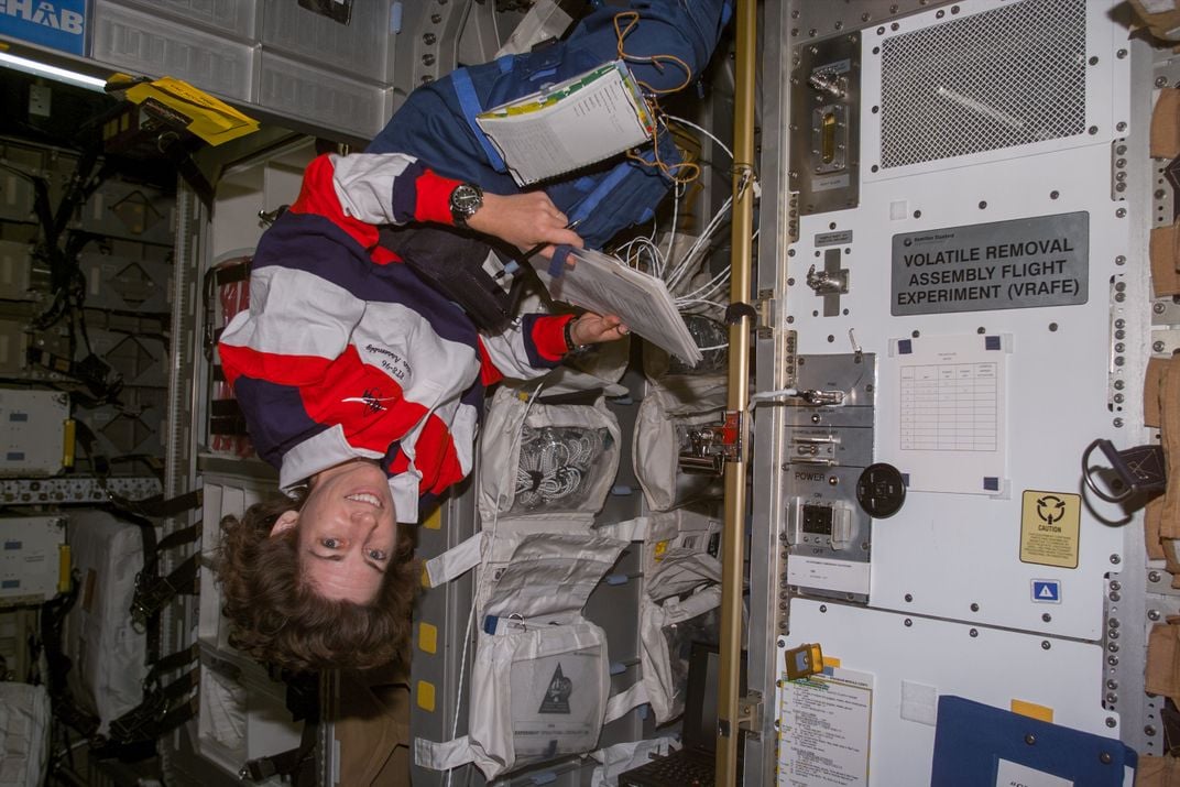 Ellen Ochoa sits upside-down in the space shuttle Discovery during an orbit of Earth, June 1999.