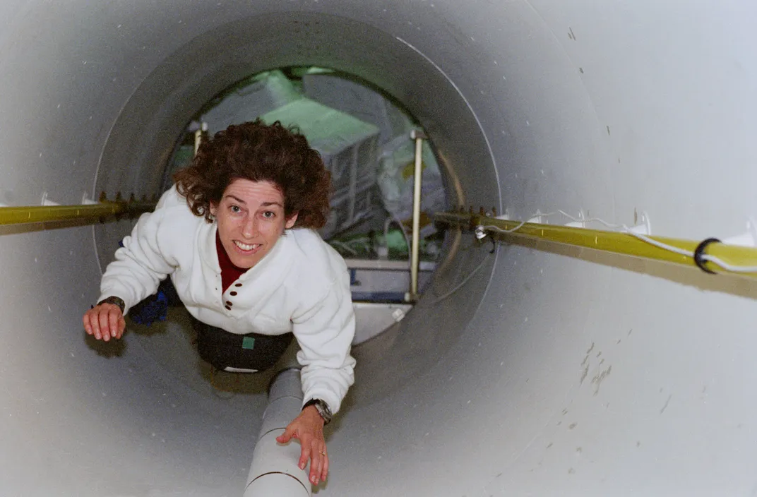 woman in white tunnel with some pipes and wiring in tubes on the walls